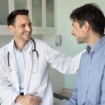 médico sorridente apoiando paciente durante consulta de saúde masculina no hospital