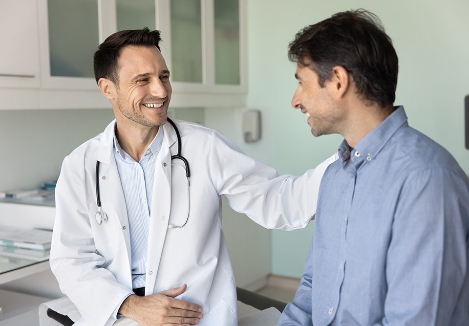 médico sorridente apoiando paciente durante consulta de saúde masculina no hospital