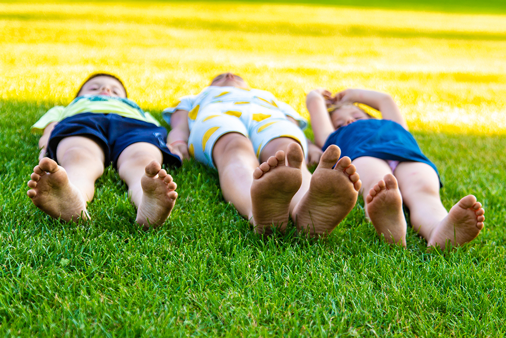 crianças deitadas na grama aproveitando um dia ensolarado ao ar livre
