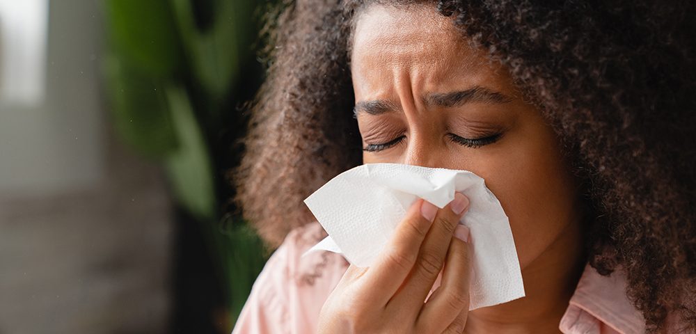 Mulher doente usando guardanapo de papel, com corrimento nasal, assoando o nariz.