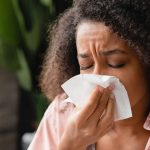Mulher doente usando guardanapo de papel, com corrimento nasal, assoando o nariz.