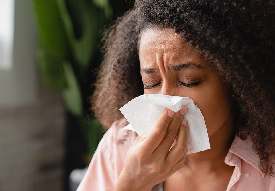 Mulher doente usando guardanapo de papel, com corrimento nasal, assoando o nariz.