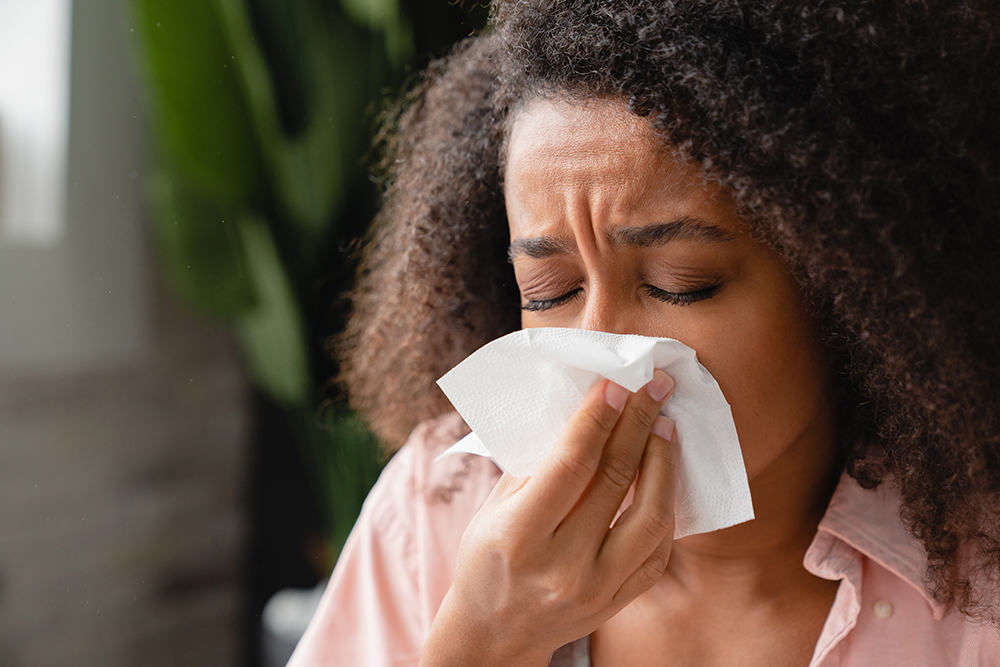 Mulher doente usando guardanapo de papel, com corrimento nasal, assoando o nariz.