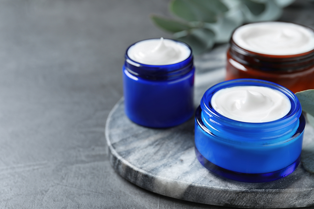 Frascos de creme hidratante em uma mesa de pedra cinza escuro.