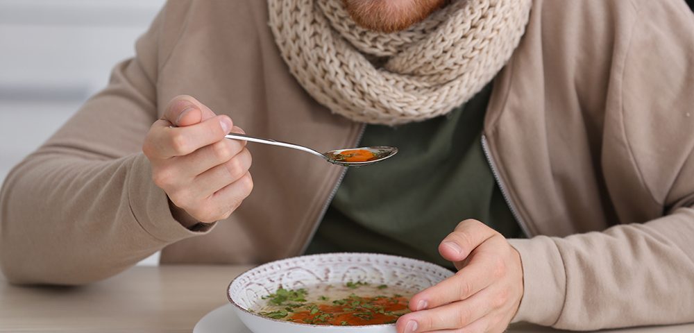 Jovem comendo na mesa dentro de casa