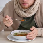 Jovem comendo na mesa dentro de casa