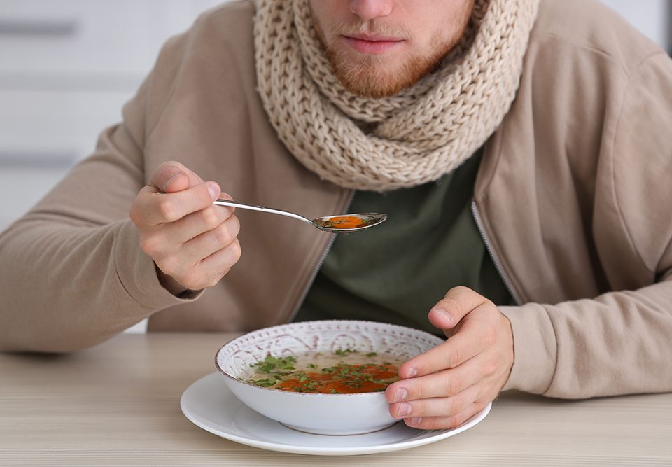 Jovem comendo na mesa dentro de casa