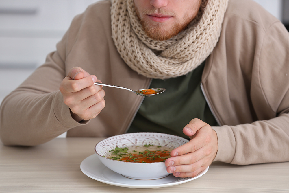 Jovem comendo na mesa dentro de casa